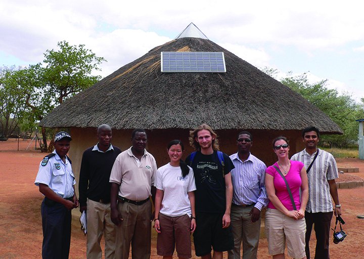 CSE students and faculty with local residents outside a traditional hut with solar panel installed