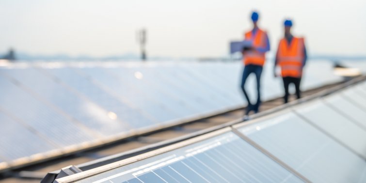 Blurred photo of two people in reflective vests walking between solar panels