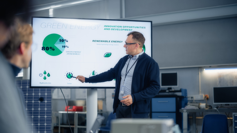 Male Engineer Points at Big Screen With Presentation and Talks About Green Energy and Solar Panels Future Possibilities