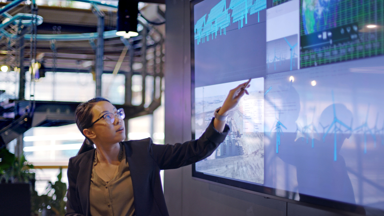 Young Asian woman points at large screen and lectures on electricity production with solar panels